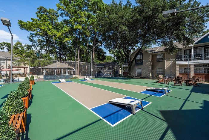 Beautiful outdoor recreation area with landscaped lawn, cornhole game boards, and inviting seating under tall trees in a serene residential complex.