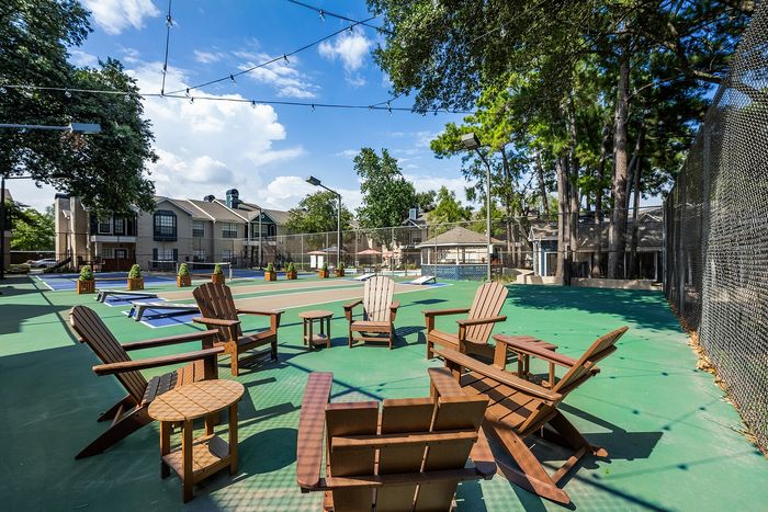 Inviting outdoor recreation area featuring stylish wooden chairs, string lights, and a tennis court, perfect for social gatherings and relaxation.