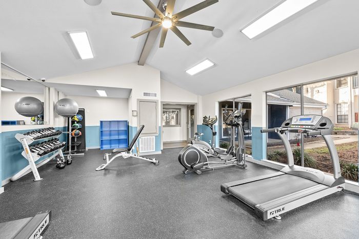 Bright and spacious gym with modern equipment, including treadmills, an elliptical, free weights, and exercise balls, featuring large windows for natural light.
