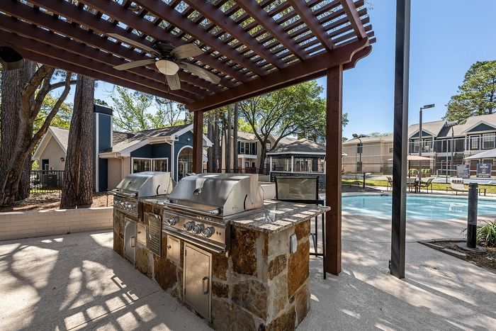 Inviting outdoor area with stylish pergola, modern barbecue grills, and a refreshing swimming pool set against a backdrop of charming architecture.