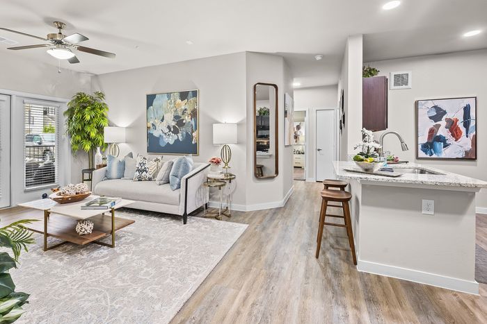 Bright and inviting open-concept living space with modern decor, featuring a cozy sofa, elegant artwork, and a sleek kitchen bar.