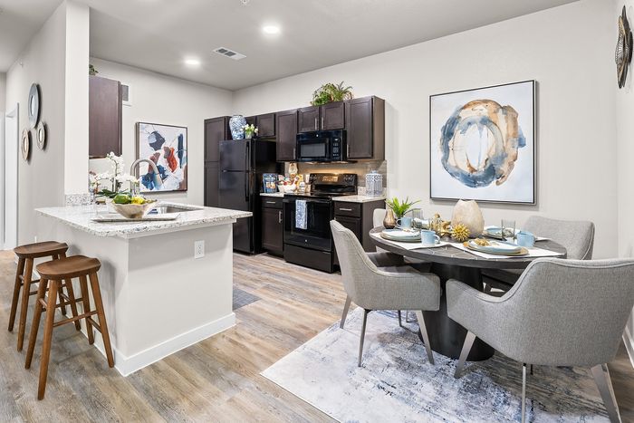 Modern kitchen and dining area with sleek dark cabinets, stylish countertops, and contemporary art on walls, creating an inviting and vibrant living space.
