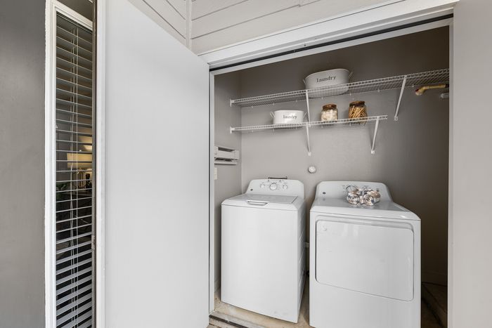 Sleek and modern laundry nook with washer, dryer, and shelving for storage in a well-lit apartment.