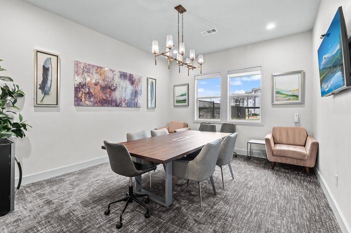 Elegant meeting room with modern decor, featuring a large wooden table, stylish gray chairs, and eye-catching artwork. Natural light fills the space through wide windows, creating an inviting atmosphere.
