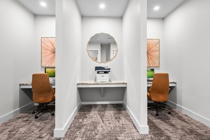 Modern office space with dual workstations featuring comfortable orange chairs, sleek marble countertops, and elegant wall art, ideal for productivity.