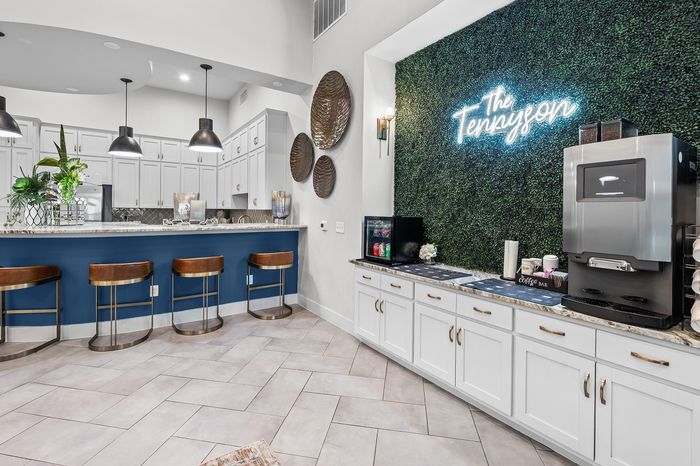 Elegant apartment kitchen with stylish bar seating, sleek white cabinets, and a lush green wall for a modern touch.