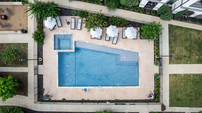 Luxurious apartment complex showcasing modern architecture, a central swimming pool, and a cozy outdoor pavilion with lush green surroundings.