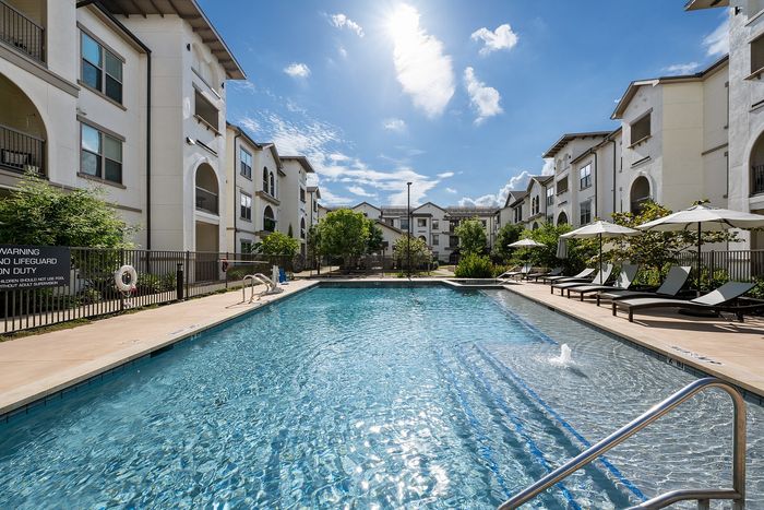 Luxurious apartment complex showcasing modern architecture, a central swimming pool, and a cozy outdoor pavilion with lush green surroundings.