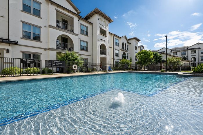 Luxurious apartment complex showcasing modern architecture, a central swimming pool, and a cozy outdoor pavilion with lush green surroundings.