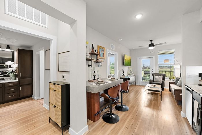 Chic apartment communal area with round tables, green seating, and panoramic nature mural, featuring a golf simulator and large windows offering serene views.