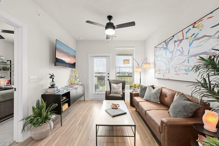 Chic apartment communal area with round tables, green seating, and panoramic nature mural, featuring a golf simulator and large windows offering serene views.