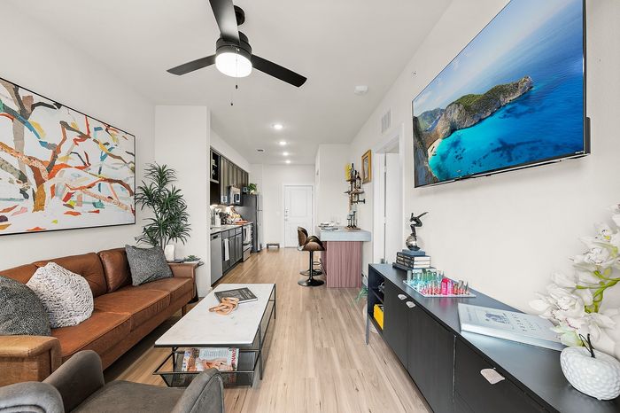 Chic apartment communal area with round tables, green seating, and panoramic nature mural, featuring a golf simulator and large windows offering serene views.