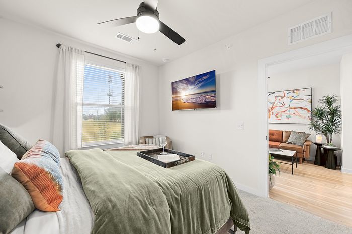 Chic apartment communal area with round tables, green seating, and panoramic nature mural, featuring a golf simulator and large windows offering serene views.