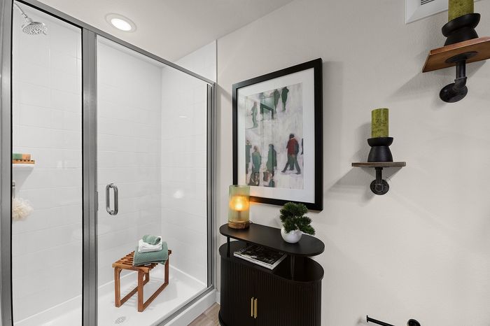 Chic apartment communal area with round tables, green seating, and panoramic nature mural, featuring a golf simulator and large windows offering serene views.