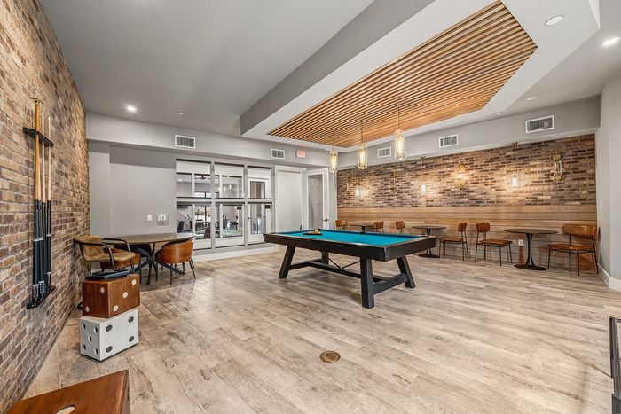 Chic recreational room with modern pool table, stylish brick walls, comfortable seating, and elegant lighting.