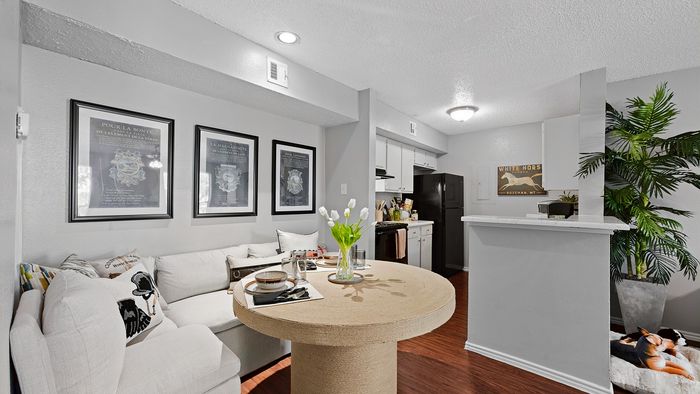 Charming living space with cozy white couch, stylish round dining table set for two, and an inviting open kitchen with modern appliances.