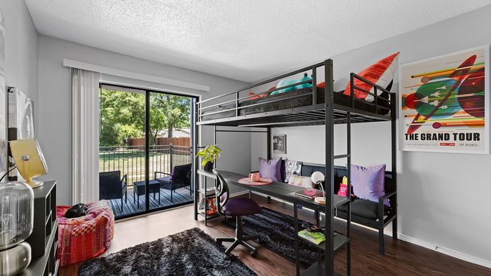 Modern apartment bedroom featuring a stylish loft bed, cozy desk area, and sliding glass doors leading to a scenic patio view.