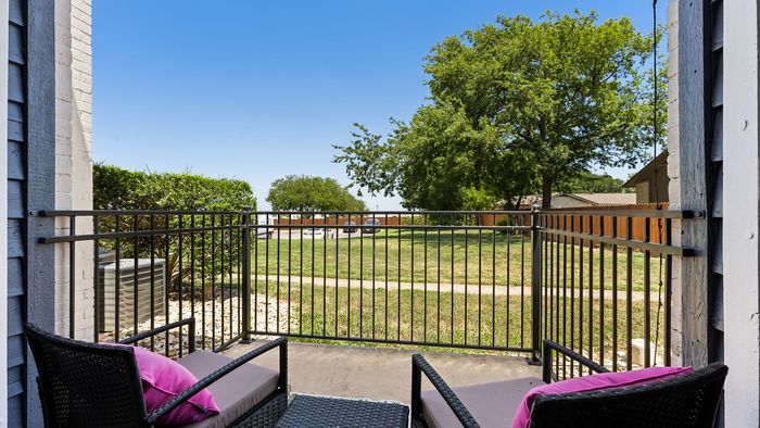 Charming balcony with cozy seating overlooking a lush green lawn, perfect for relaxing and enjoying the serene outdoor views.