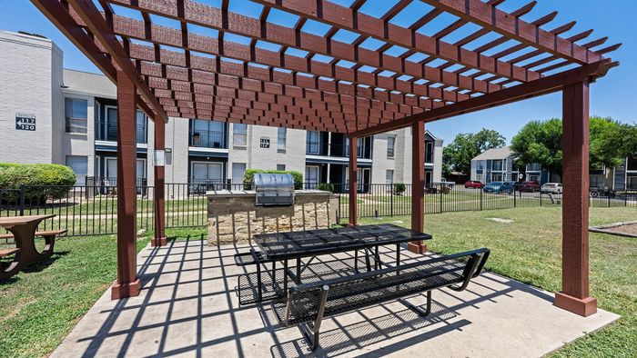Inviting outdoor area featuring a charming pergola with a picnic table and grill, perfect for alfresco dining in a serene apartment community.