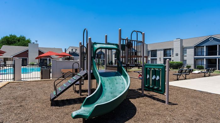 Inviting community playground next to a refreshing pool area with stylish apartments in the background.