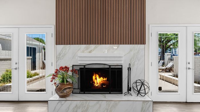 Elegant living room fireplace with modern marble surround, warm fire, and stylish decor, adjacent to glass doors opening to a sunny patio.