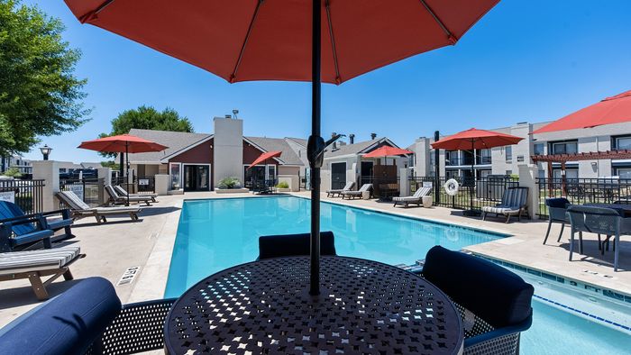 Inviting swimming pool area with stylish lounge chairs and vibrant red umbrellas, perfect for relaxation and leisure.