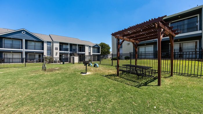 Charming apartment complex featuring a lush grassy courtyard with a picnic area and stylish pergola, perfect for outdoor gatherings.