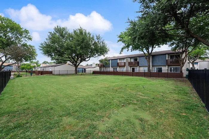 Expansive green lawn with scenic landscaping, showcasing modern apartment buildings and mature trees under a vibrant blue sky.