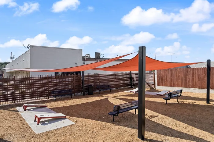 Inviting outdoor area featuring modern shade sails, comfortable benches, and vibrant cornhole boards for leisure activities.