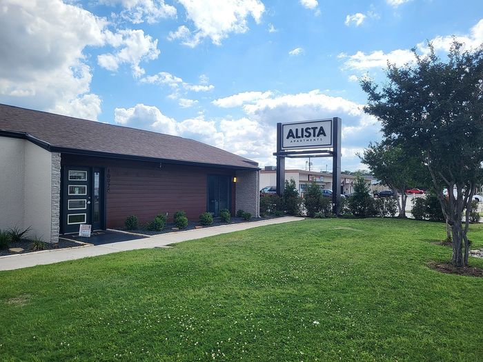 Charming Alista Apartments exterior with lush green lawn, modern architecture, and inviting entrance on a bright sunny day.