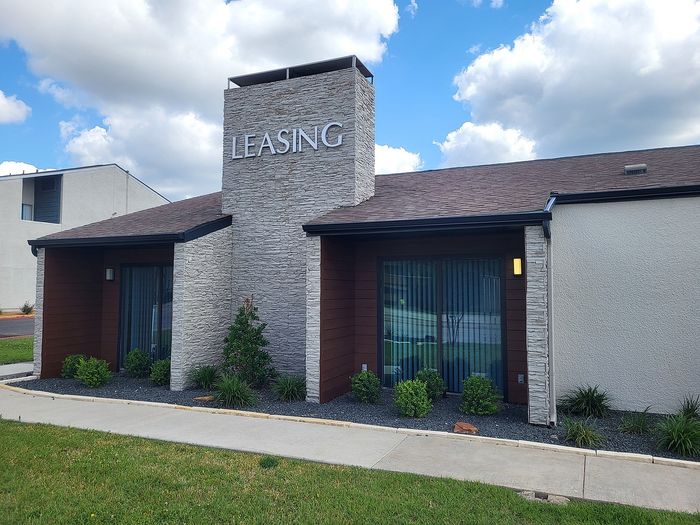 Modern leasing office exterior featuring elegant stonework, large windows, and lush landscaping under a vibrant blue sky.