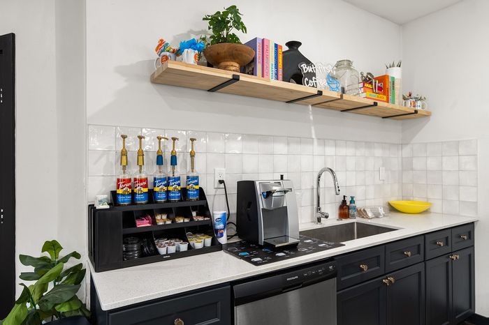 Modern kitchenette setup with a sleek coffee maker, syrup dispensers, and decorative shelving, perfect for coffee enthusiasts.