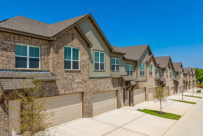 Charming row of modern townhouses with brick facades and spacious double garages on a sunny day.