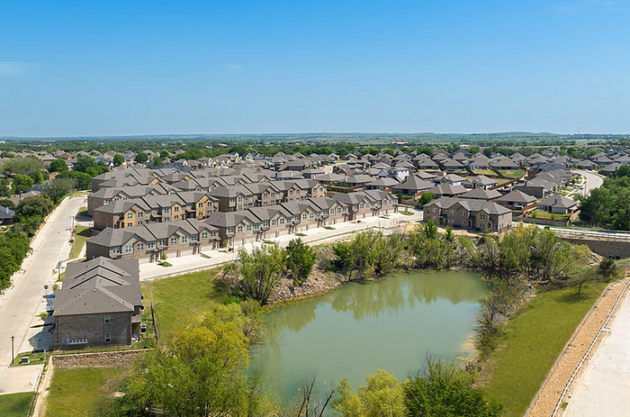 Aerial view of a picturesque neighborhood with modern townhouses nestled around a serene pond, showcasing a peaceful living environment.