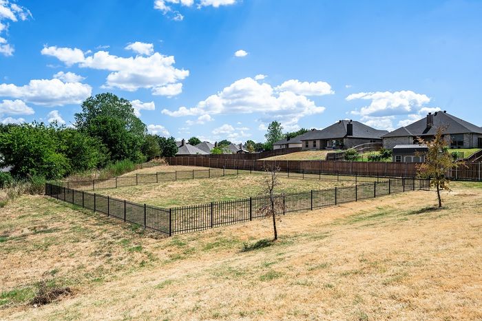 Spacious fenced dog park with scenic views, offering a perfect area for outdoor activities and relaxation, under a bright blue sky with scattered clouds.