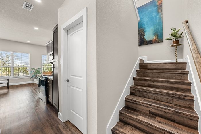 Bright and inviting apartment with open-plan kitchen, large windows, and elegant wooden staircase leading to second floor.