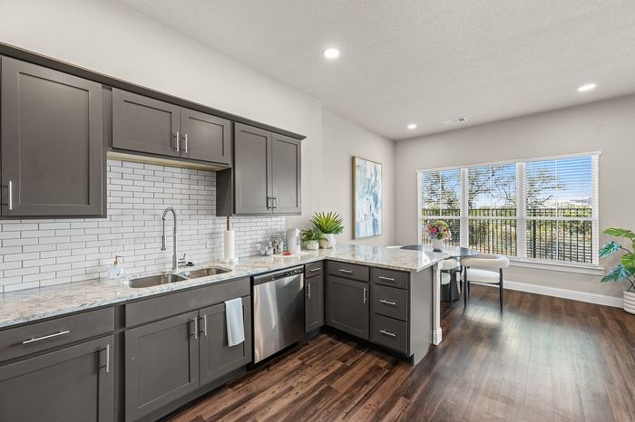 Modern kitchen with sleek gray cabinets, marble countertops, and bright natural light from large windows, creating an inviting dining space.