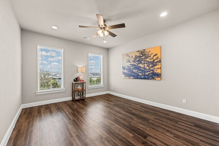 Inviting room with elegant hardwood floors, large windows for natural light, and modern ceiling fan, perfect for relaxation or creativity.