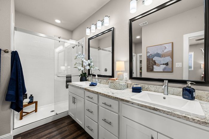 Luxurious bathroom featuring dual sinks with elegant mirrors, a modern glass shower, and stylish decor with soft lighting.