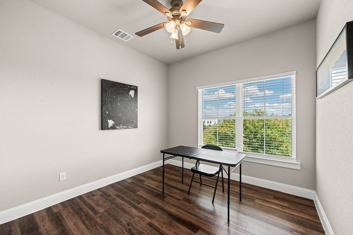 Bright, minimalistic home office with a large window, elegant ceiling fan, and sleek hardwood flooring.