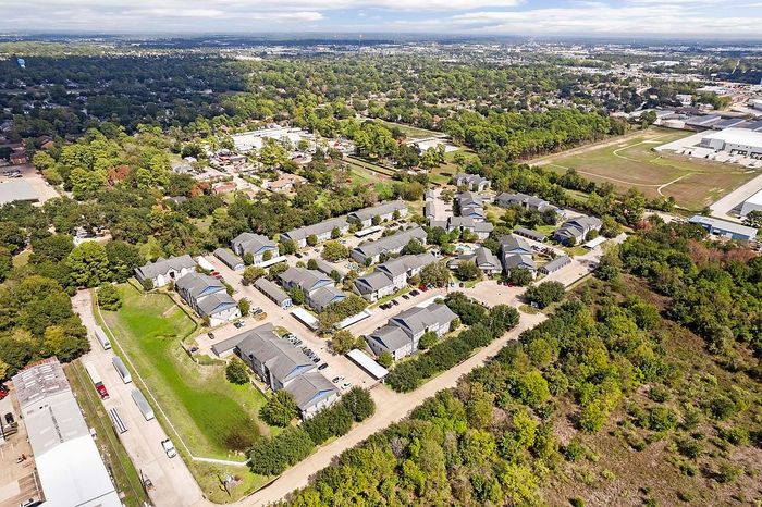 Charming aerial view of a serene suburban apartment community, nestled amidst lush greenery and offering a peaceful, family-friendly environment with convenient access to nearby amenities.