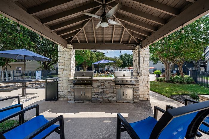 Charming outdoor pavilion with dual stainless steel grills, surrounded by stone columns and lush greenery, perfect for entertaining.