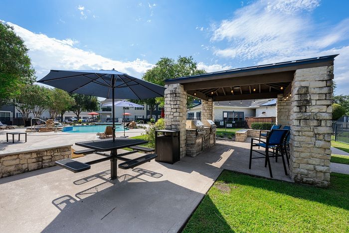 Inviting outdoor space with a covered barbecue area, modern seating, and a refreshing pool under a clear blue sky.