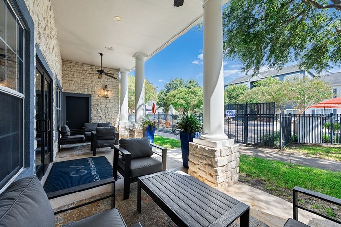 Charming patio with cozy seating and stone fa&ccedil;ade, overlooking lush greenery and a closed pool area.