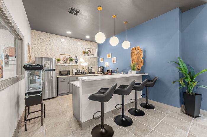Modern kitchen with sleek gray cabinetry, stylish black bar stools, and elegant pendant lighting against a vibrant blue accent wall.