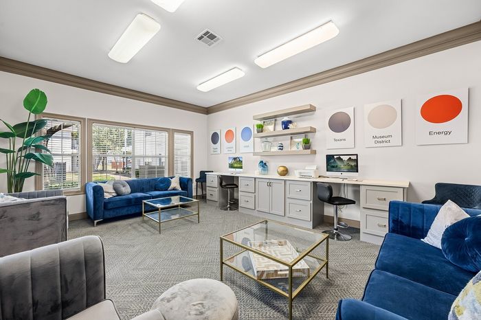 Chic lounge area with plush blue couches, modern glass tables, and a functional work desk, perfect for relaxation and productivity.