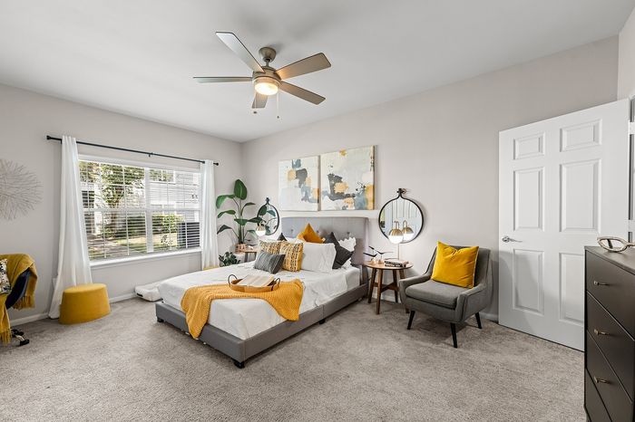 Inviting bedroom with modern decor, cozy bed, stylish accent chair, and large window for ample natural light.