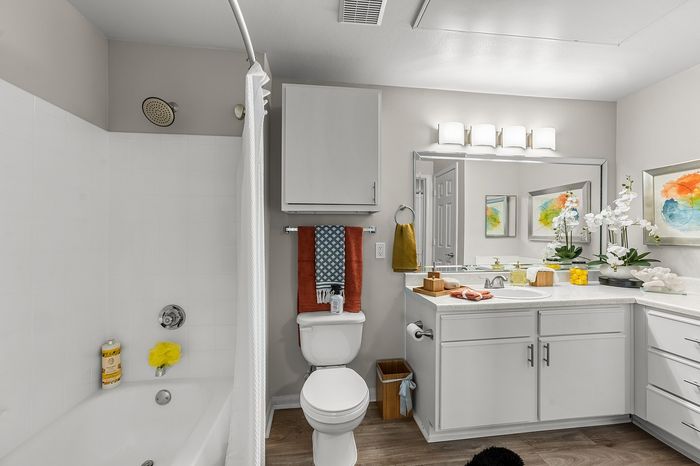 Modern bathroom featuring sleek white cabinetry, elegant mirror lighting, and vibrant artwork, offering a spa-like atmosphere.