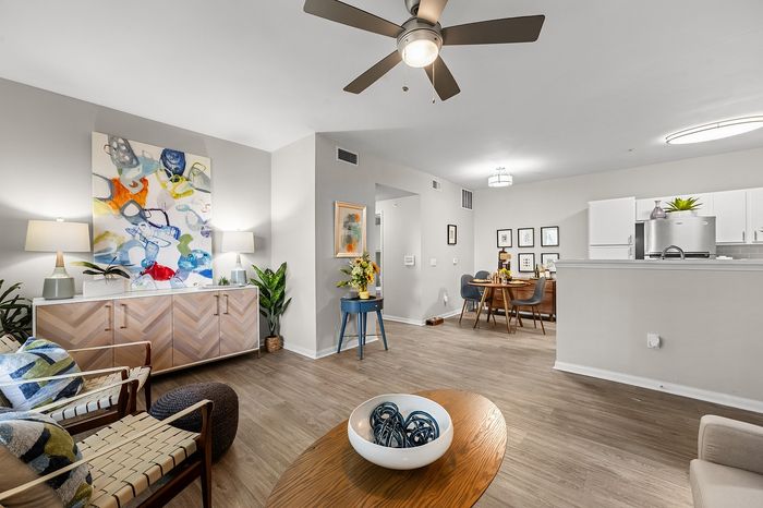 Modern living area with stylish decor, featuring a colorful abstract painting, cozy seating, and a glimpse of the dining and kitchen spaces.