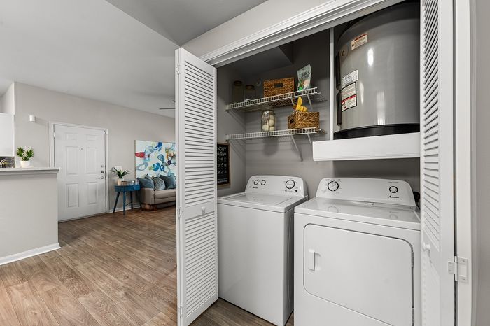 Modern apartment interior showcasing a convenient in-unit laundry area with washer and dryer, adjacent to a chic living room with vibrant decor and sleek flooring.